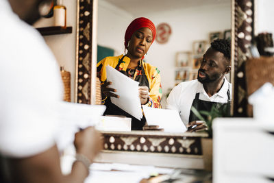 Mature female barber discussing over paper document with male coworker at hair salon