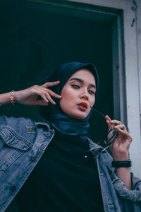 Portrait of young woman holding camera while standing outdoors