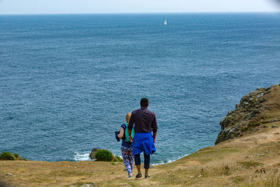 Rear view of friends walking on hill by sea against sky