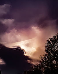 Low angle view of silhouette trees against storm clouds