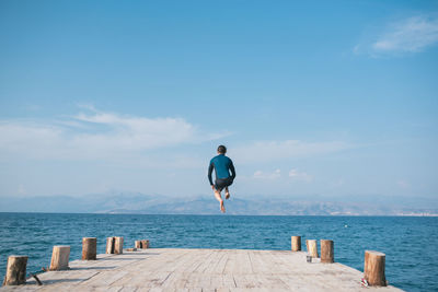 Rear view of man on pier over sea against sky