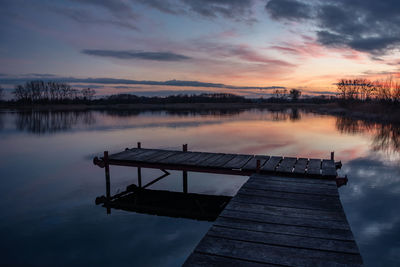 Fishing pier over a calm lake and beautiful sunset on the sky