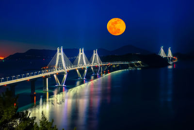 Illuminated suspension bridge over river against sky at night