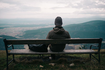 Rear view of man sitting on bench against landscape