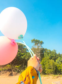 Midsection of person holding balloons against blue sky