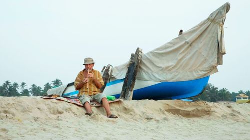 Rear view of man sitting on beach against clear sky