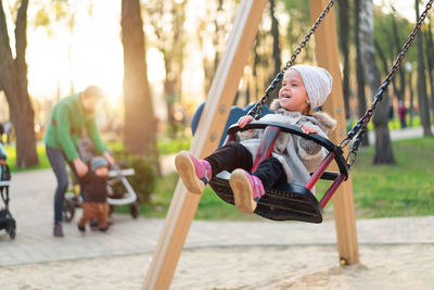 Cheerful cute girl sitting on swing at playground