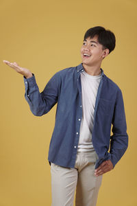 Young man looking away while standing against yellow background