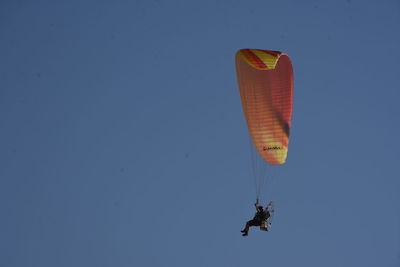 Low angle view of people paragliding against clear sky