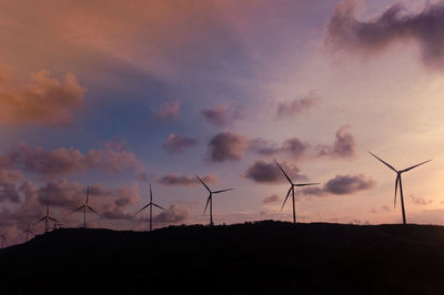 Silhouette wind turbines on field against sky during sunset