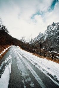 Snow covered road by trees against sky