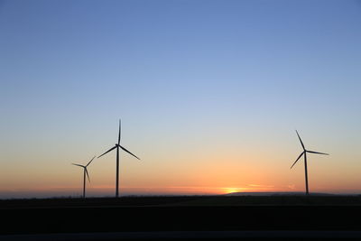 Silhouette wind turbines on landscape against romantic sky at sunset