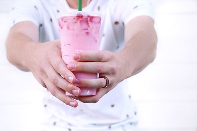 Midsection of person offering pink cold drink against white background