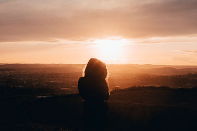 Silhouette woman standing on landscape against sky during sunset