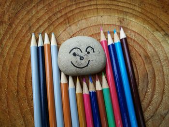 High angle view of stone with anthropomorphic face by colored pencils on wooden table