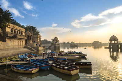 Boats moored in river by buildings against sky