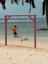 A boy playing swing on the beach in the morning