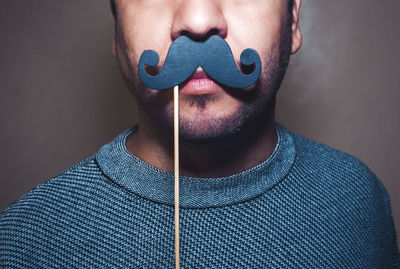 Close-up of man with prop mustache against gray background