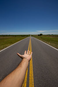 Cropped image of hand on road against clear blue sky