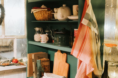 Green kitchen rack with shelves and kitchen utensils. kettle, mugs, cutting boards, towels