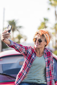 Young woman using mobile phone while standing against car