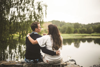 Rear view of romantic couple sitting on retaining wall against lake