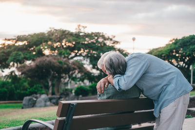 Side view of man sitting on bench against trees