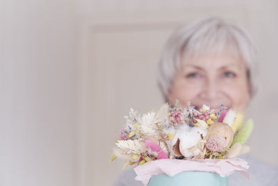 A portrait of an elderly caucasian woman with short gray hair with a bouquet of dried flowers