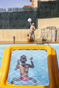 Two kids playing with a ball on a pool