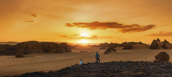 People on rocks at beach against sky during sunset