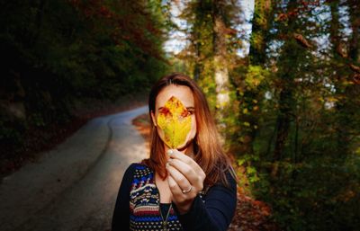 Woman holding autumn leaf against trees in forest
