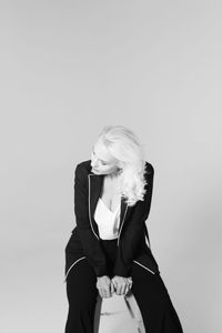 Businesswoman sitting on stool against gray background