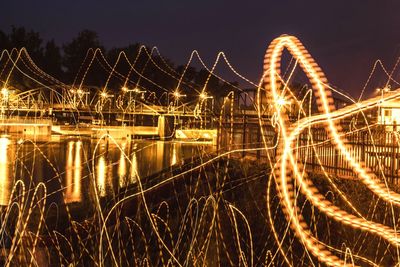 Light trails on bridge over river against sky at night