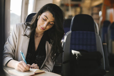 Businesswoman with long hair writing on diary while sitting in train