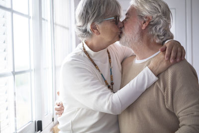 Senior couple kissing while standing by window at home