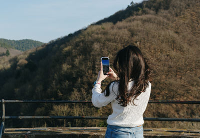 Side view of young woman photographing while standing against mountain
