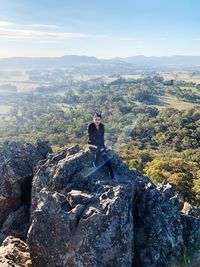 Man sitting on rock against sky