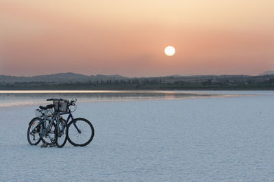 Bicycle by lake against sky during sunset