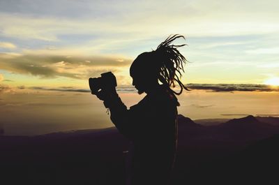 Silhouette man photographing against sky during sunset