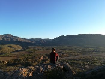 Women sitting on mountain against clear blue sky