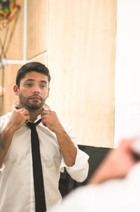 Reflection of man getting dressed while standing at home in mirror