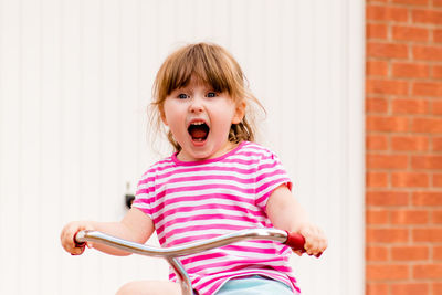 Portrait of girl screaming while riding bicycle against wall
