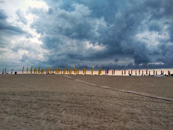 Distant view of closed parasols at beach against storm clouds