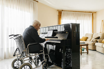 Senior man sitting in wheelchair playing piano at home