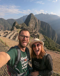 Portrait of smiling friends sitting on mountain against sky in machucado picchu