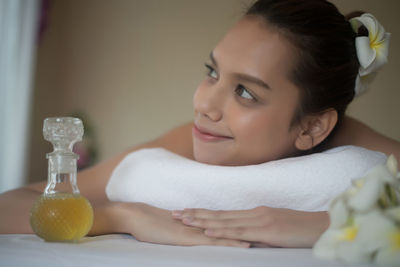Smiling young woman by oil lying on massage table in spa