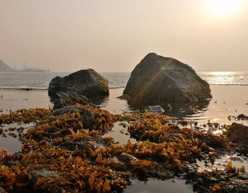 Rock formation on beach against sky during sunrise 