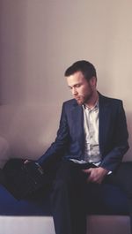 Businessman using laptop while sitting on sofa against wall in office