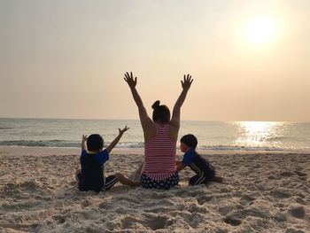 Rear view of mother with children at beach against sky during sunset