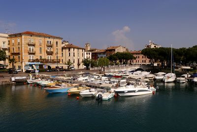 Sailboats moored on harbor by buildings against sky in city